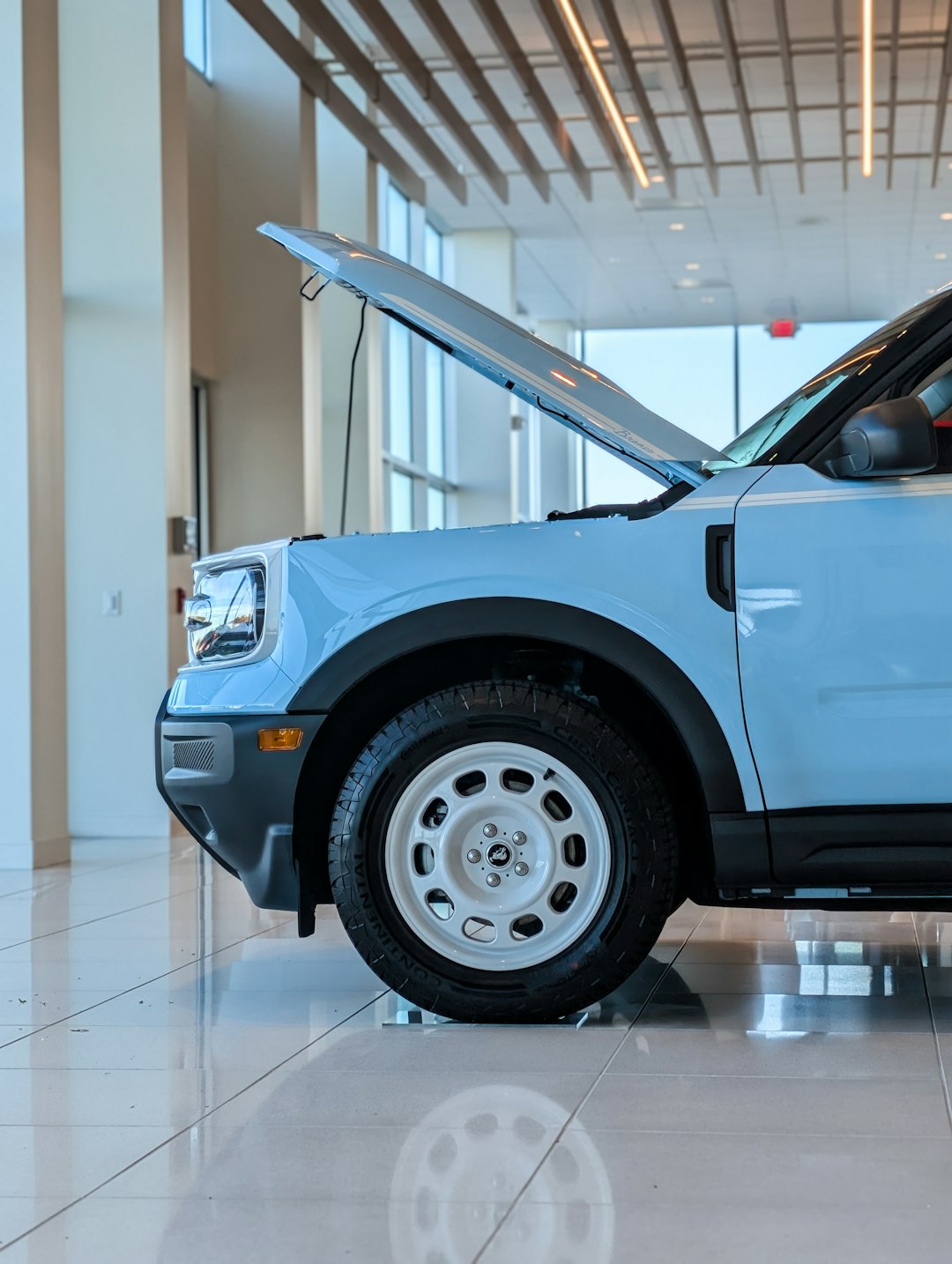 This gorgeous profile shot highlights the striking contrast of the pastel blue body and retro white wheel against the pristine, highly reflective showroom floor, with the raised hood inviting admiration of its capable engineering. Boulevard Ford in Millsboro