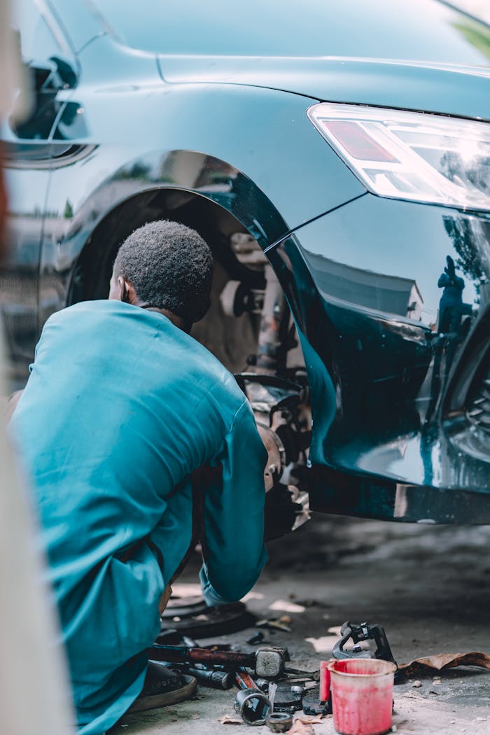 An adult male mechanic working on car brake repair at an auto garage.