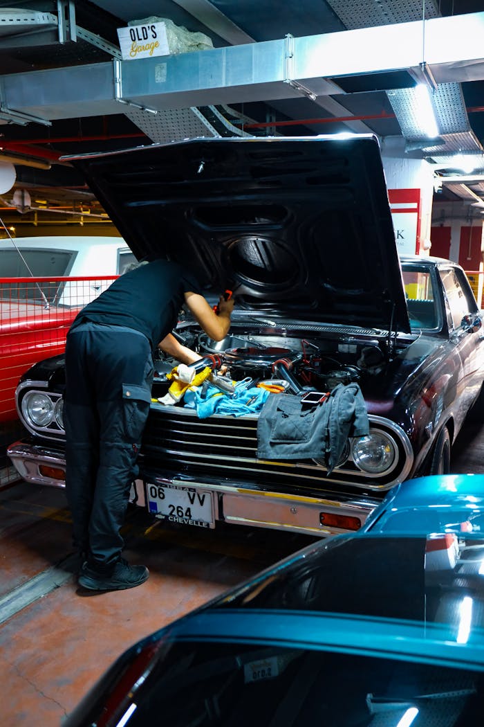 A mechanic works on a classic car engine in a dimly lit garage setting.